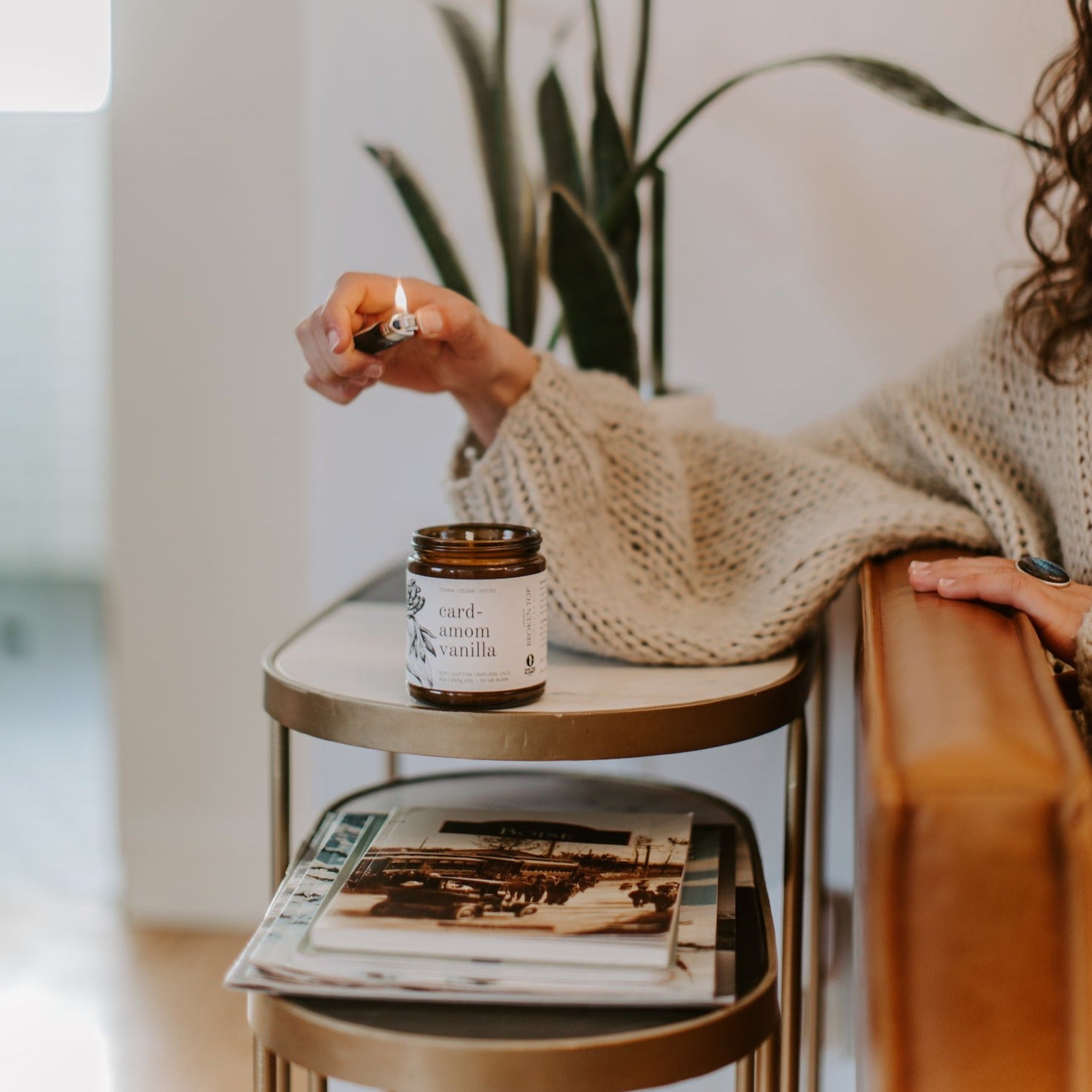 9oz Cardamom Vanilla Soy Candle on a side table being lit by a lighter. 