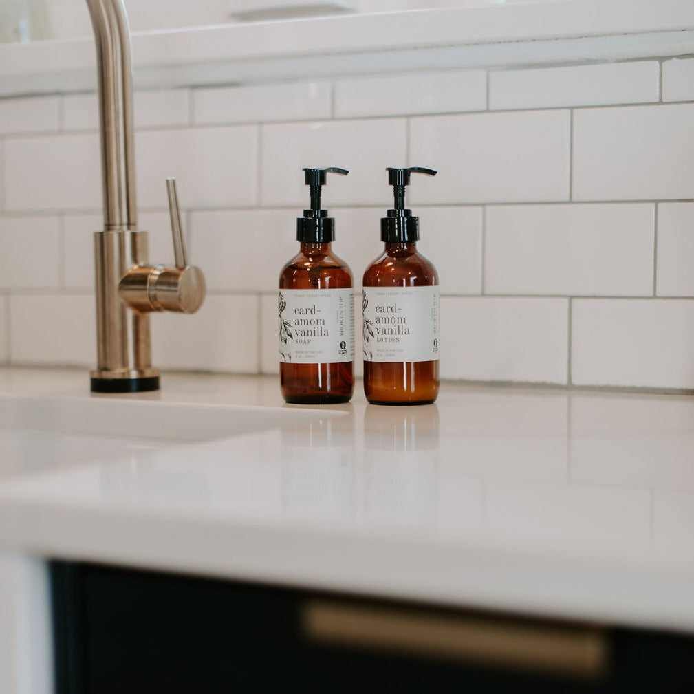 8oz Cardamom Vanilla Liquid Soap and 8oz Cardamom Vanilla Body Lotion next to a kitchen sink. 