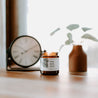 4oz Sea Salt Surf Soy Candle on a table next to a clock and small plant. 