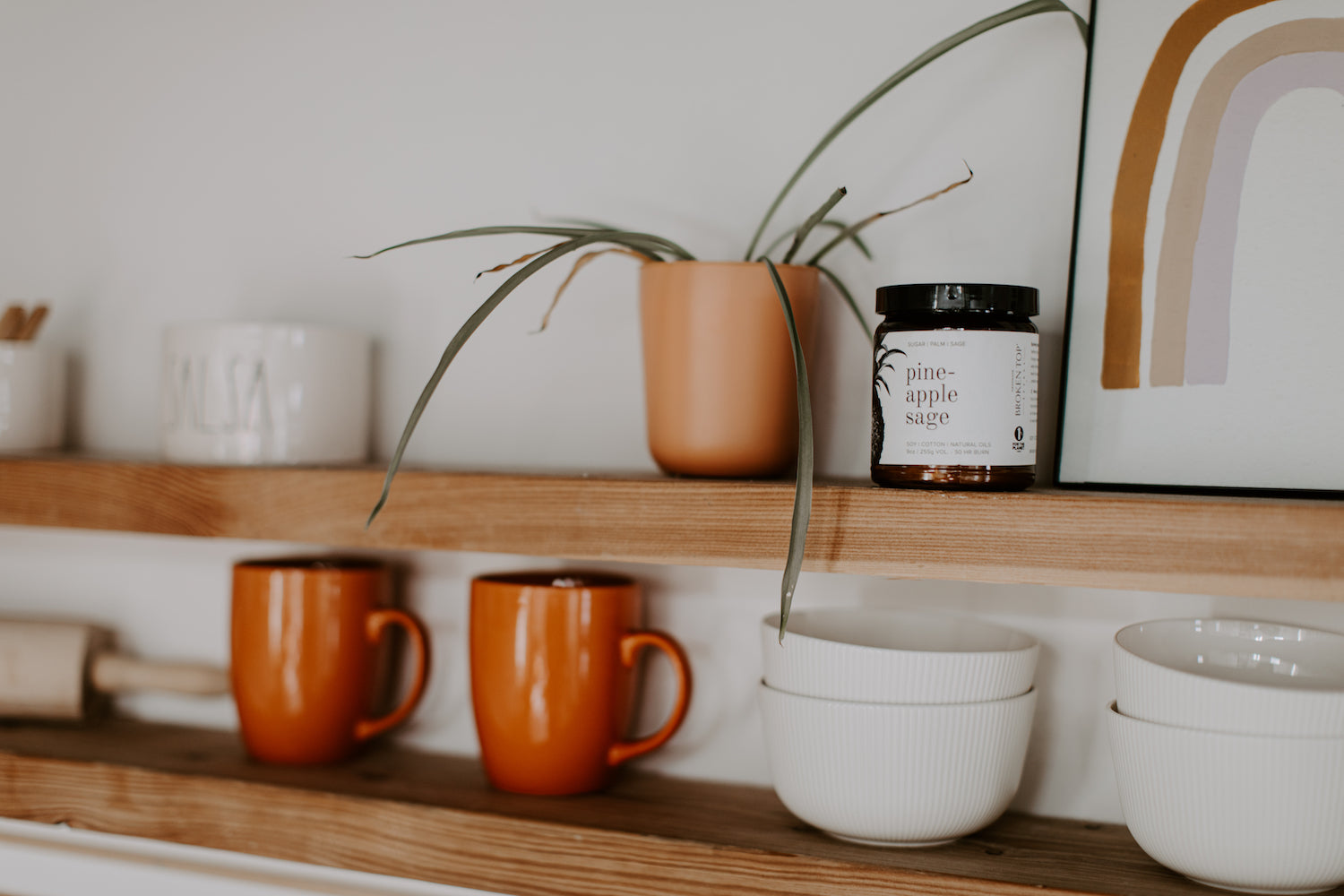 9oz Pineapple Sage Soy Candle on a kitchen shelf next to ceramic mugs and bowls. 