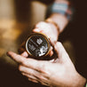 Tobacco Teak Solid Cologne being held by two hands. 