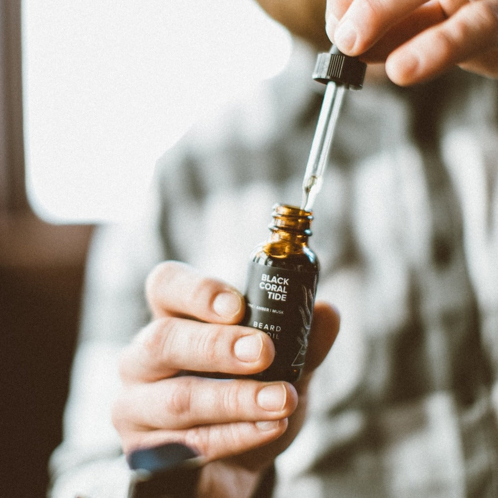 1oz Black Coral Tide Beard Oil being held by two hands. 