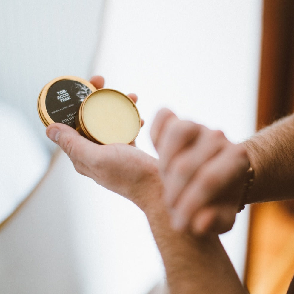 Tobacco Teak Solid Cologne being applied with two hands. 