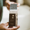 Birch Charcoal Bar Soap being taken out of the box by two hands. 
