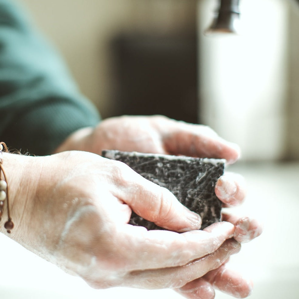 Birch Charcoal Bar Soap being rubbed together by two hands. 