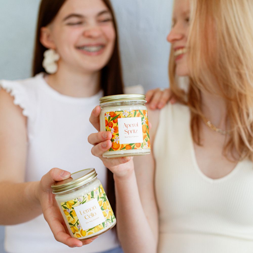 Two young women holding 9oz Lemon Cello and Aperol Spritz Soy Candles. 