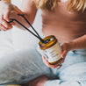 9oz Apricot Bloom Soy Candle with woman trimming the wick. 