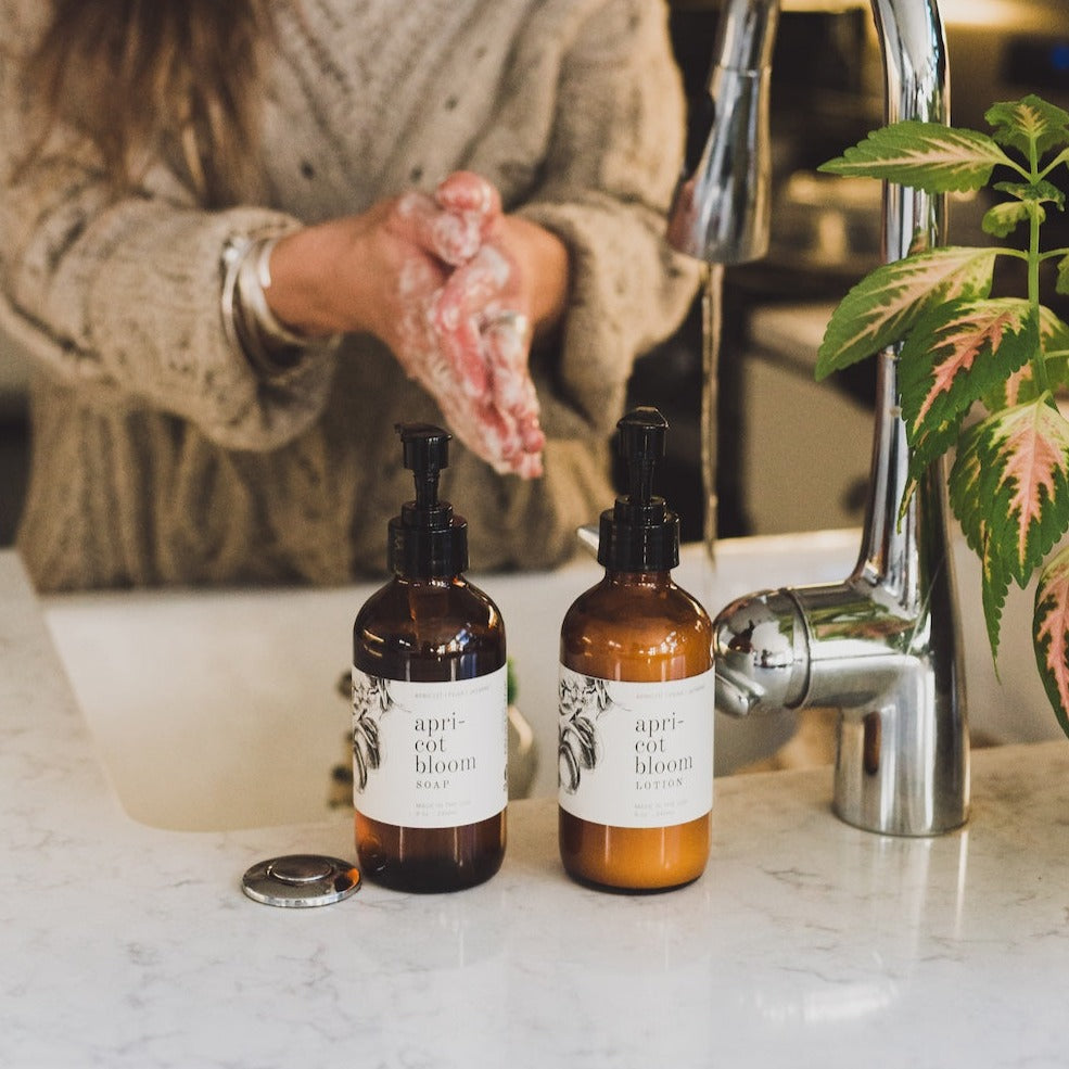 8oz Apricot Bloom Body Lotion next to 8oz Apricot Bloom Liquid Soap on kitchen countertop near the sink. 
