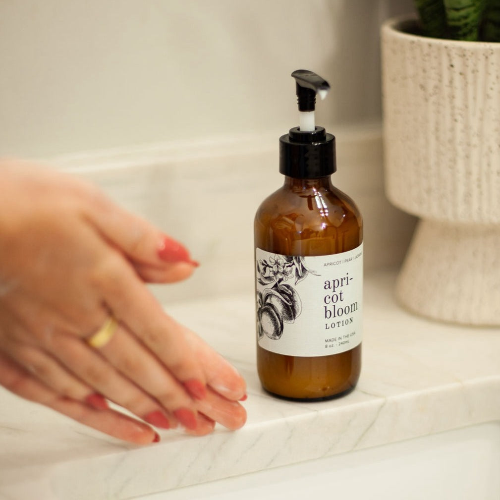 8oz Apricot Bloom Body Lotion on countertop next to two hands using lotion. 
