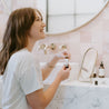 Apricot Bloom Roll-On Perfume being held by a woman sitting at a bathroom counter. 