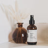 4oz Apricot Bloom Linen Spray on a countertop with small vase. 