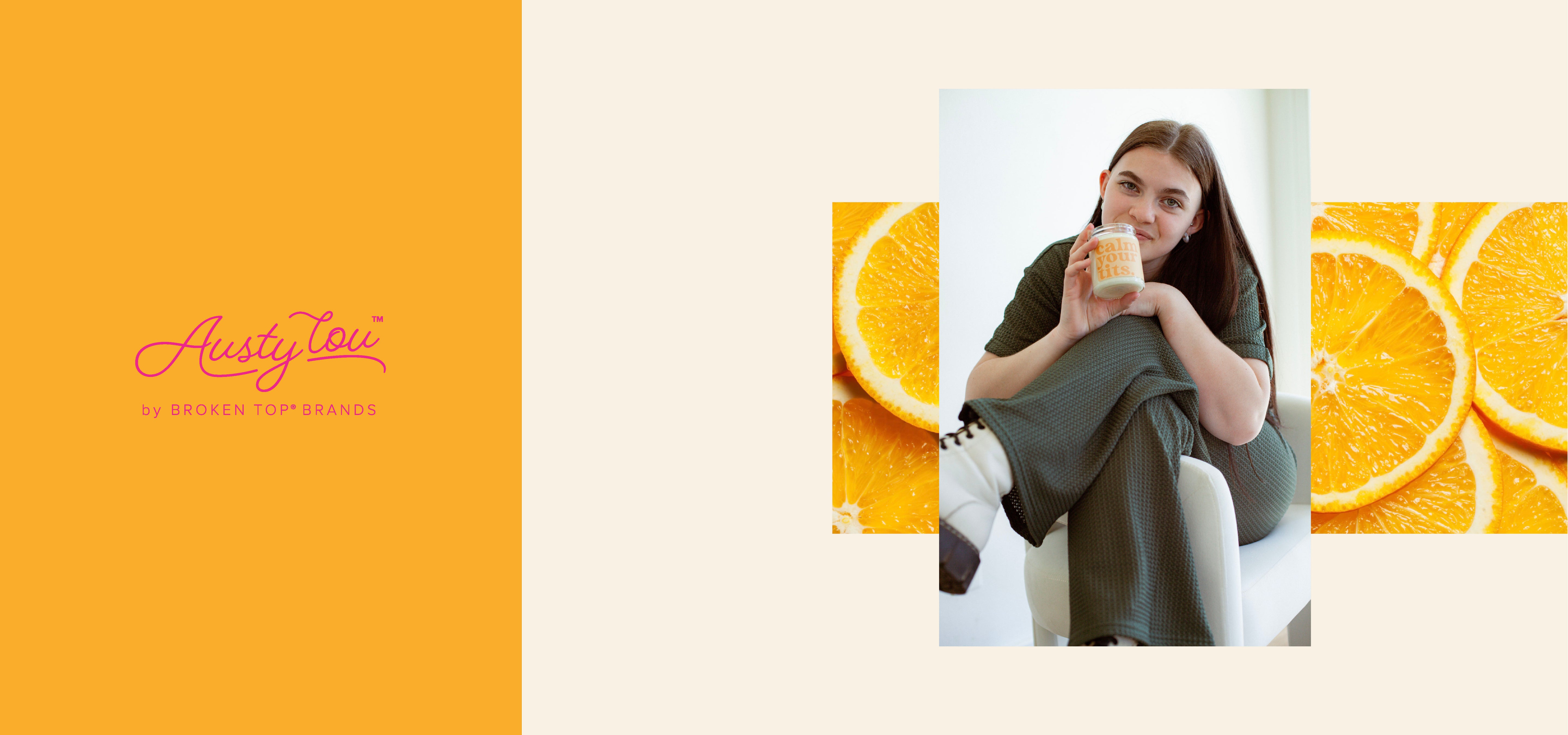 Austy Lou by Broken Top Brands logo. Young woman holding 9oz 'Calm Your Tits' Soy Candle on background of orange slices. 