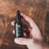 1oz Black Coral Tide Beard Oil being held by a hand. 