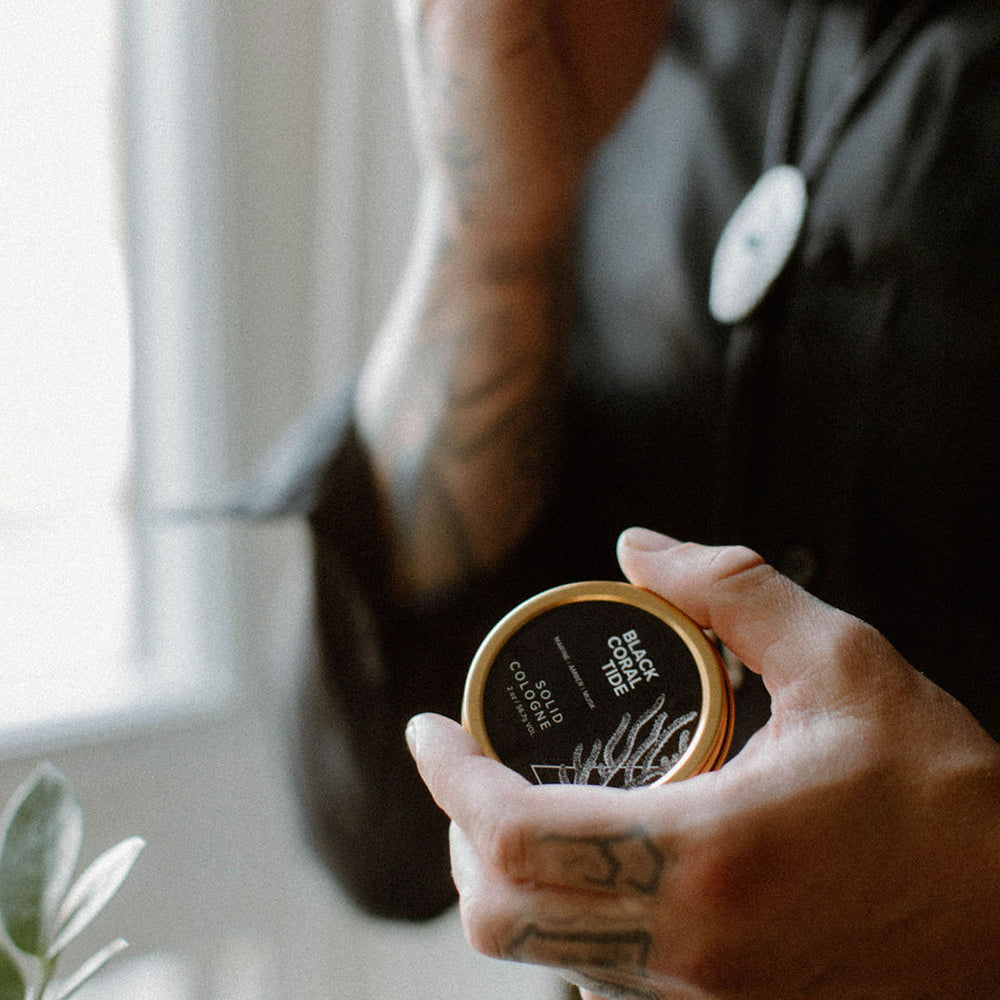 Black Coral Tide Solid Cologne being held by a man's hand. 