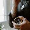 Black Coral Tide Solid Cologne being held by a man's hand. 