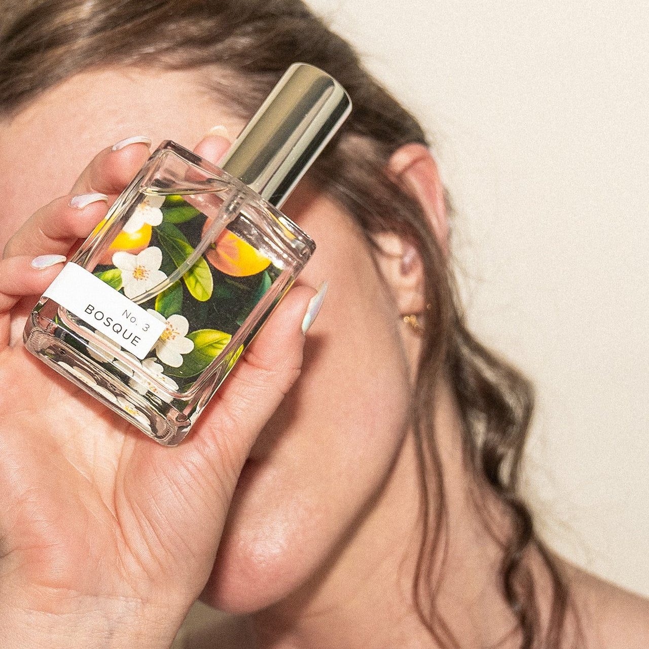 Woman holding Bosque Perfume in front of her face.