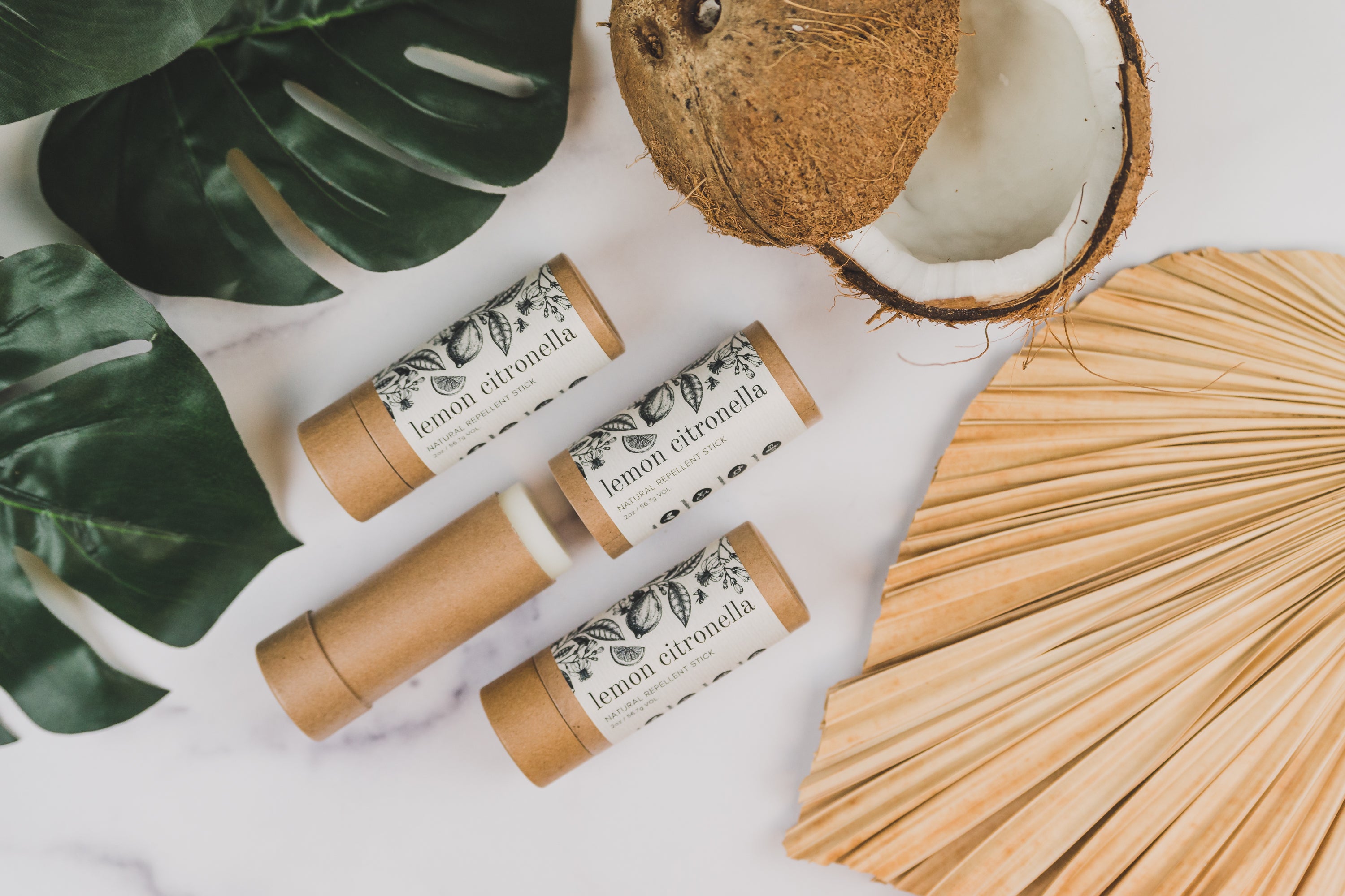 Three Lemon Citronella Repellent Sticks laid out next to decorative plants and a coconut. 