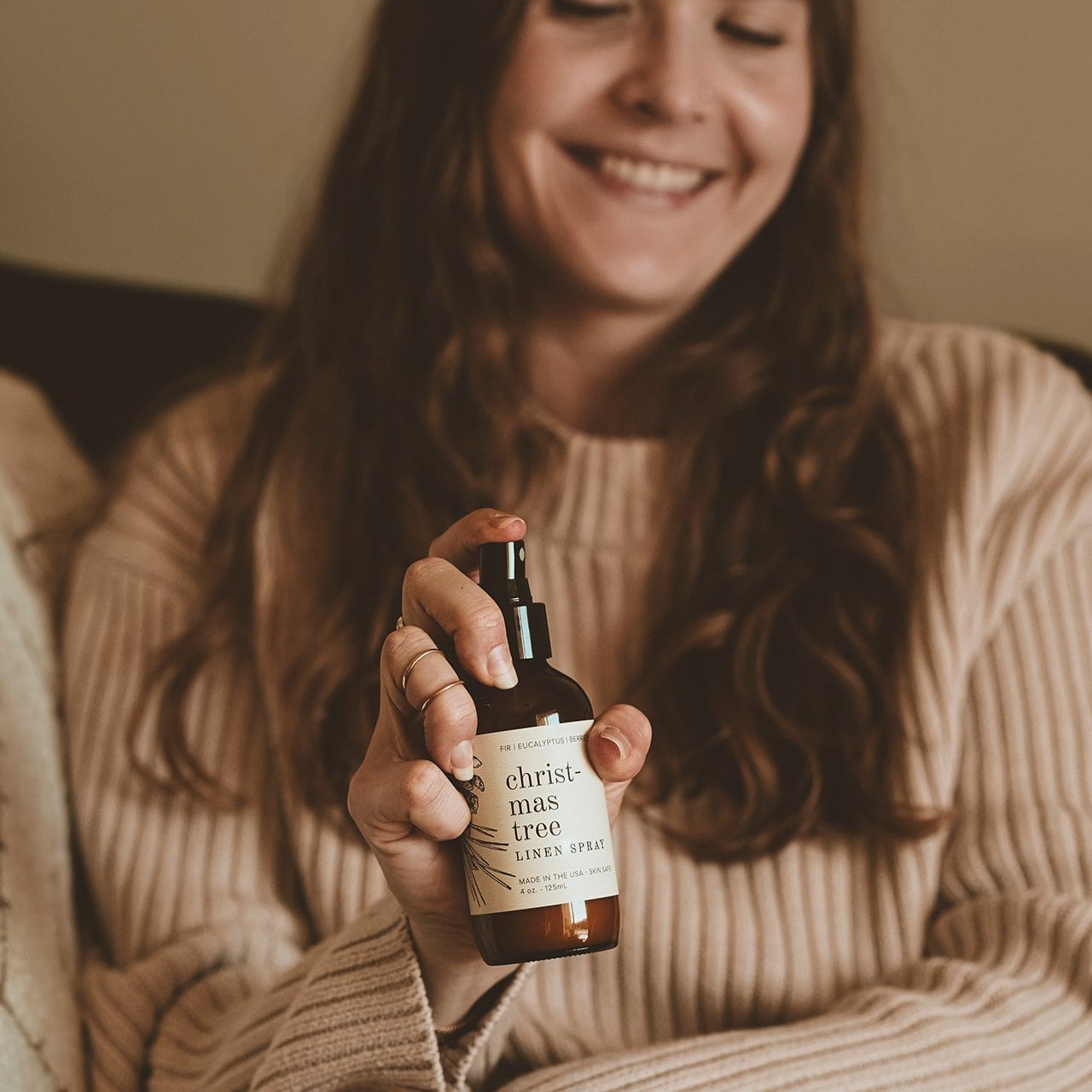 4oz Christmas Tree Linen Spray being sprayed by a woman with long brown hair. 