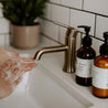8oz Christmas Tree Liquid Soap next to a bathroom sink where two hands are being washed. 