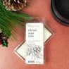 Christmas Tree Soy Wax Melt on red table next to pinecones, fir sprigs, and a black wax melter. 