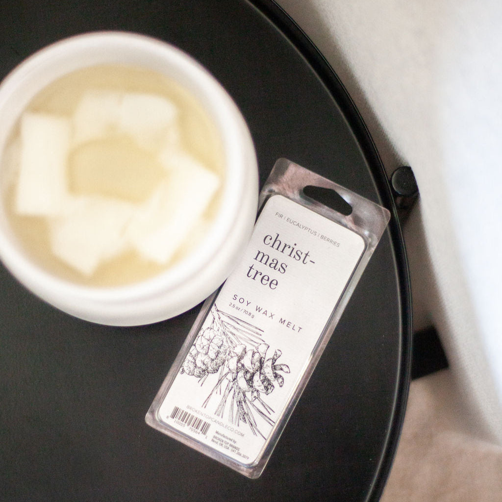 Christmas Tree Soy Wax Melt on black side table next to white wax melter. 