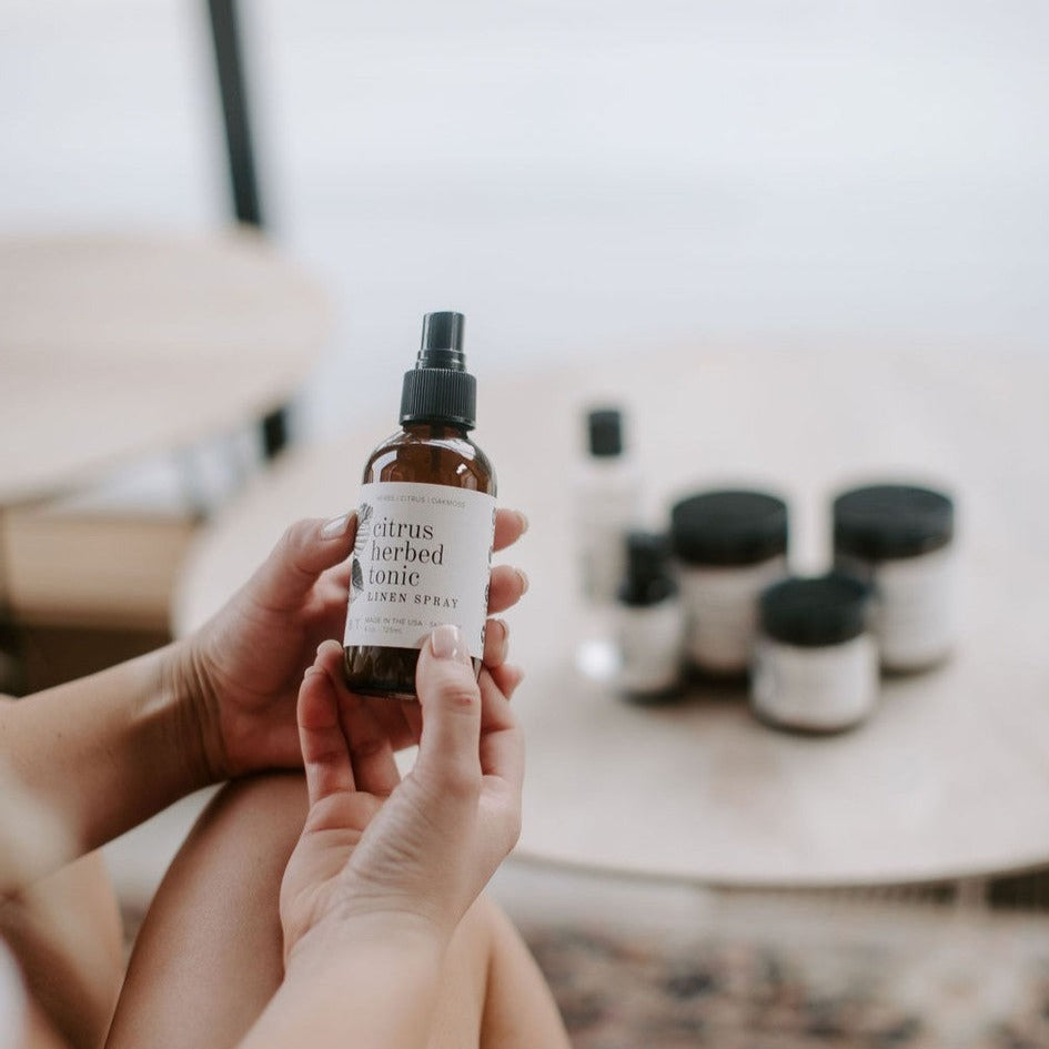 4oz Citrus Herbed Tonic Linen Spray being held by two hands. 