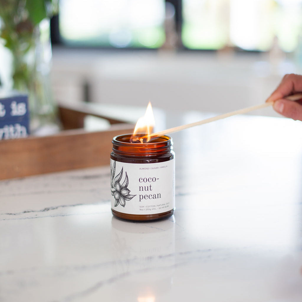 9oz Coconut Pecan Soy Candle being lit on a marble countertop. 