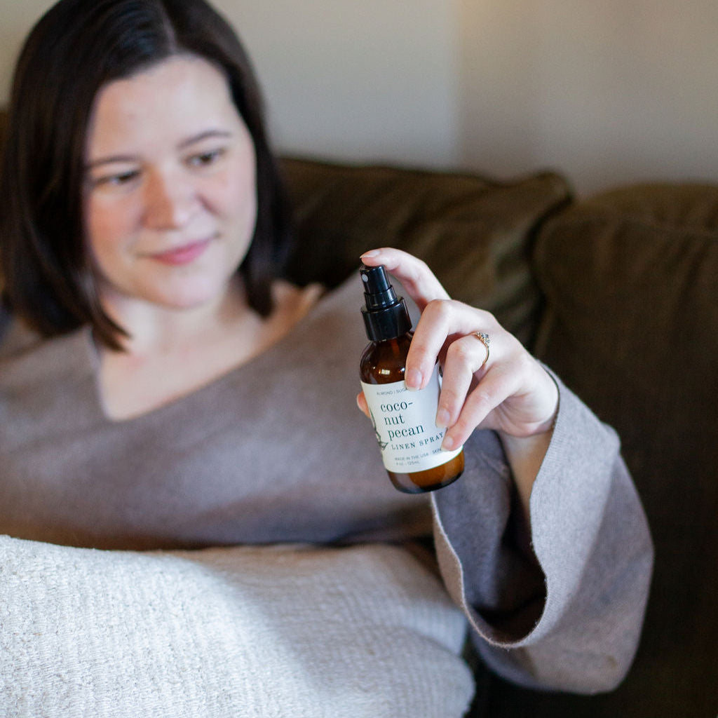 4oz Coconut Pecan Linen Spray being sprayed by a woman. 