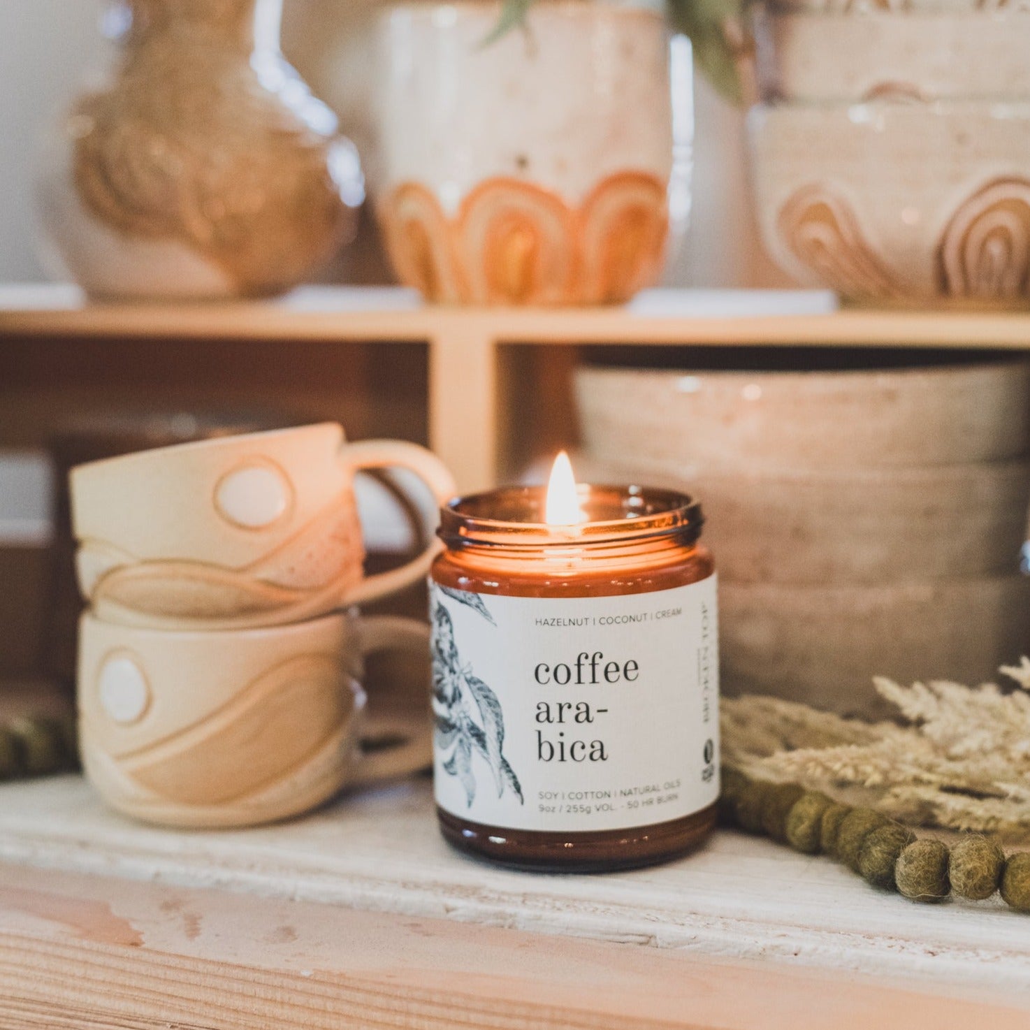 9oz Coffee Arabica Soy Candle on a shelf next to ceramic coffee mugs. 