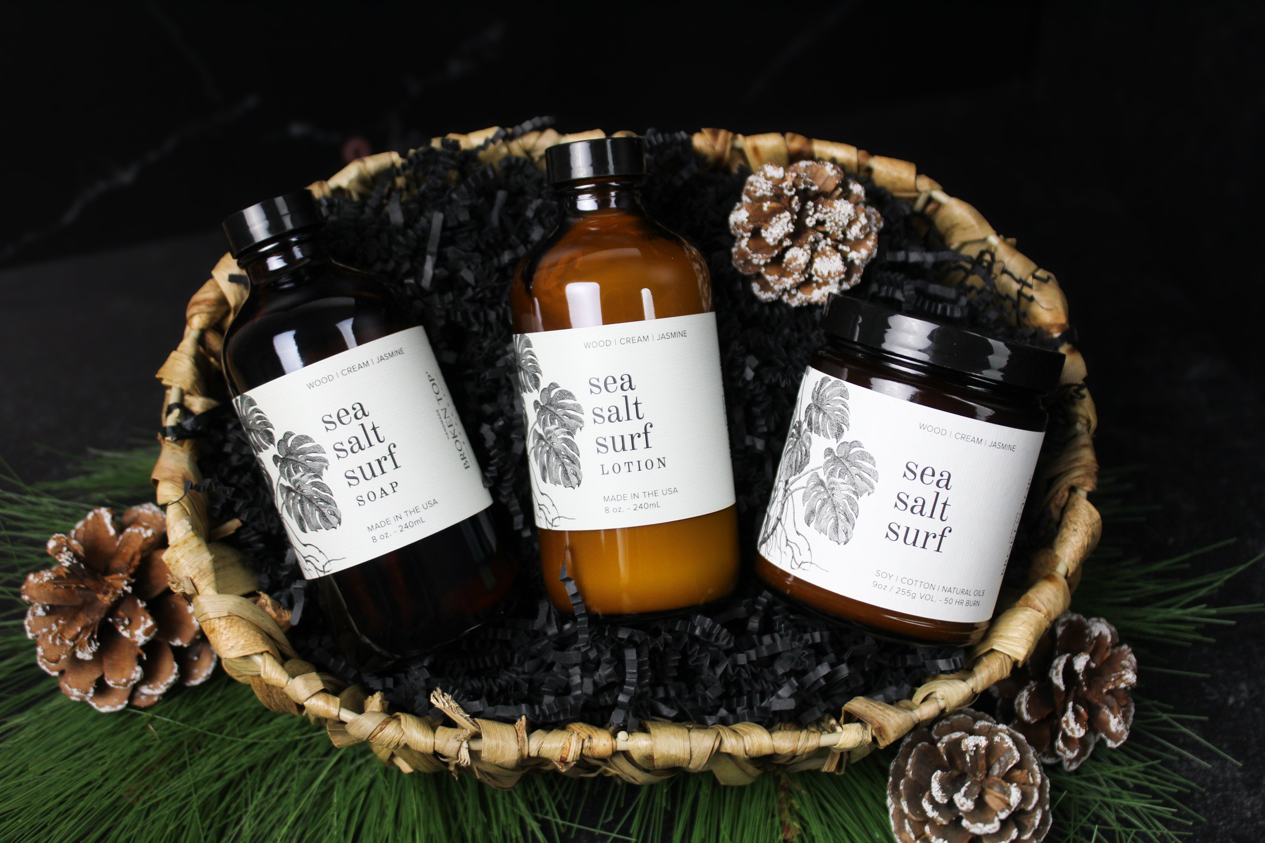 Sea Salt Surf Lotion, Liquid Soap, and Soy Candle in a gift basket surrounded by pinecones. 