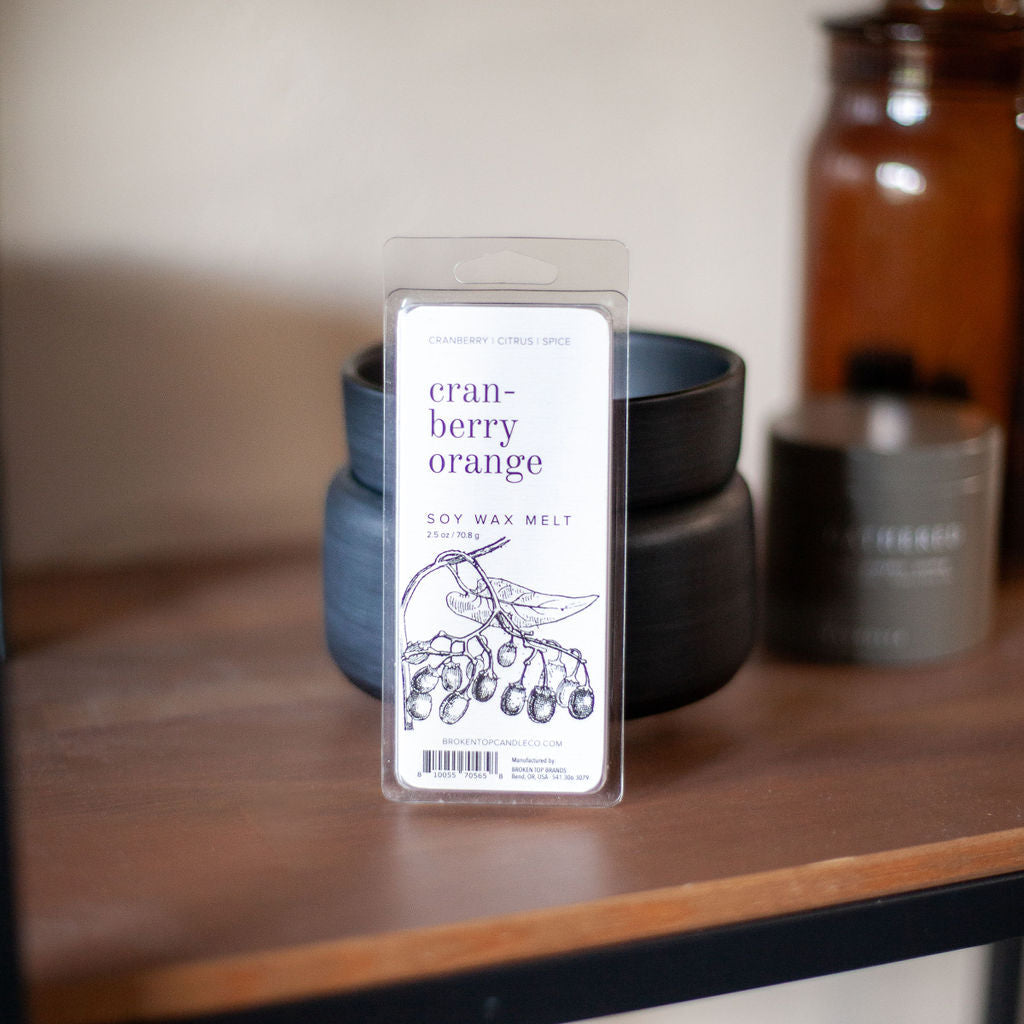 Cranberry Orange Soy Wax Melt on wooden table in front of a black wax melters. 