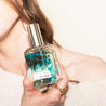 Hand holding Del Mar Perfume in front of neck. 