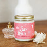9oz 'Stay Wild' Soy Candle on a wooden table next to decorative glass jar and flowers. 