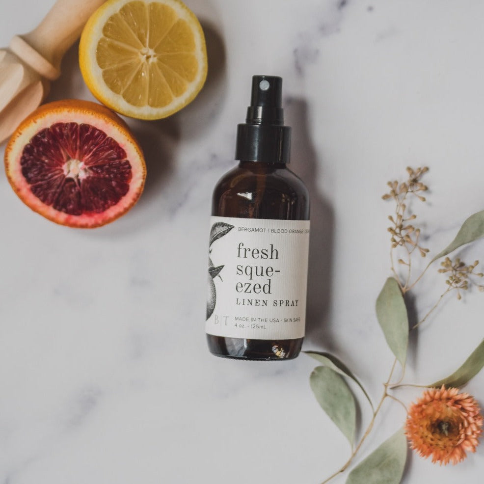 4oz Fresh Squeezed Linen Spray on marble next to sliced citrus. 