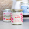 'In My Mom Era' 9oz Soy Candle on wooden side table in front of other candles. 