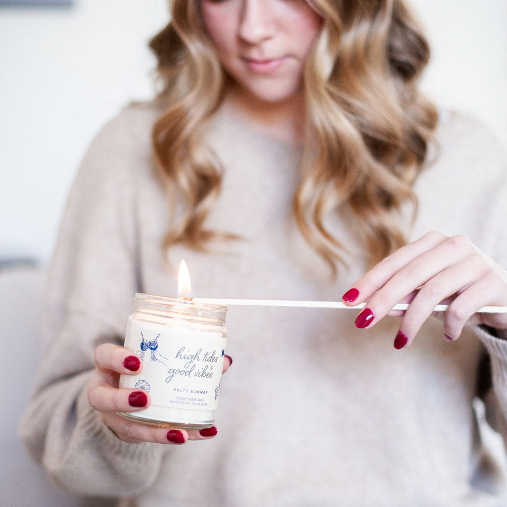 'High Tides & Good Vibes' 9oz Soy Candle being lit by a woman. 