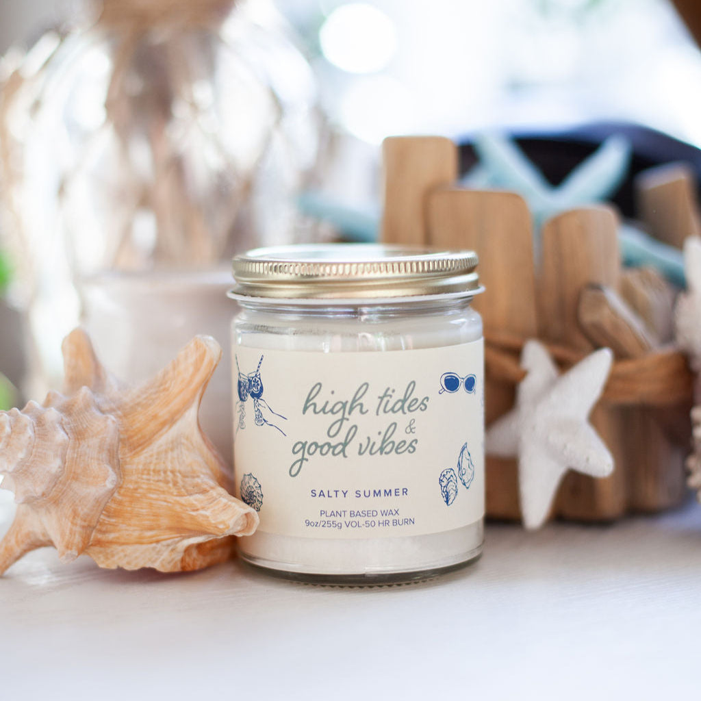 'High Tides & Good Vibes' 9oz Soy Candle next to sea shells. 