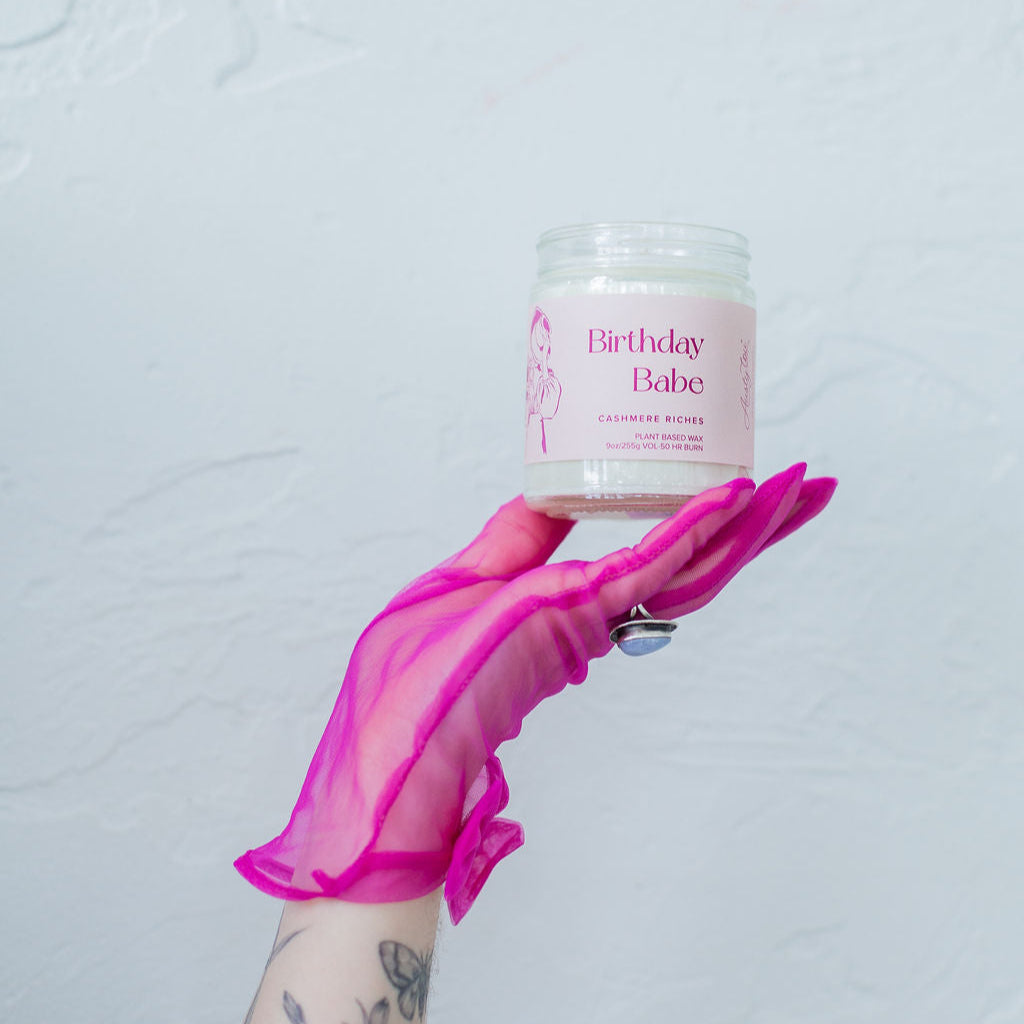 'Birthday Babe' 9oz Soy Candle being held by a hand in a pink glove. 