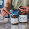 9oz and 4os Maple Harvest Soy Candles on countertop being lit by a match. 