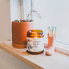 9oz Mount Bachelor Soy Candle on a window sill next to a ceramic pot and a cowboy boot shaped match holder. 