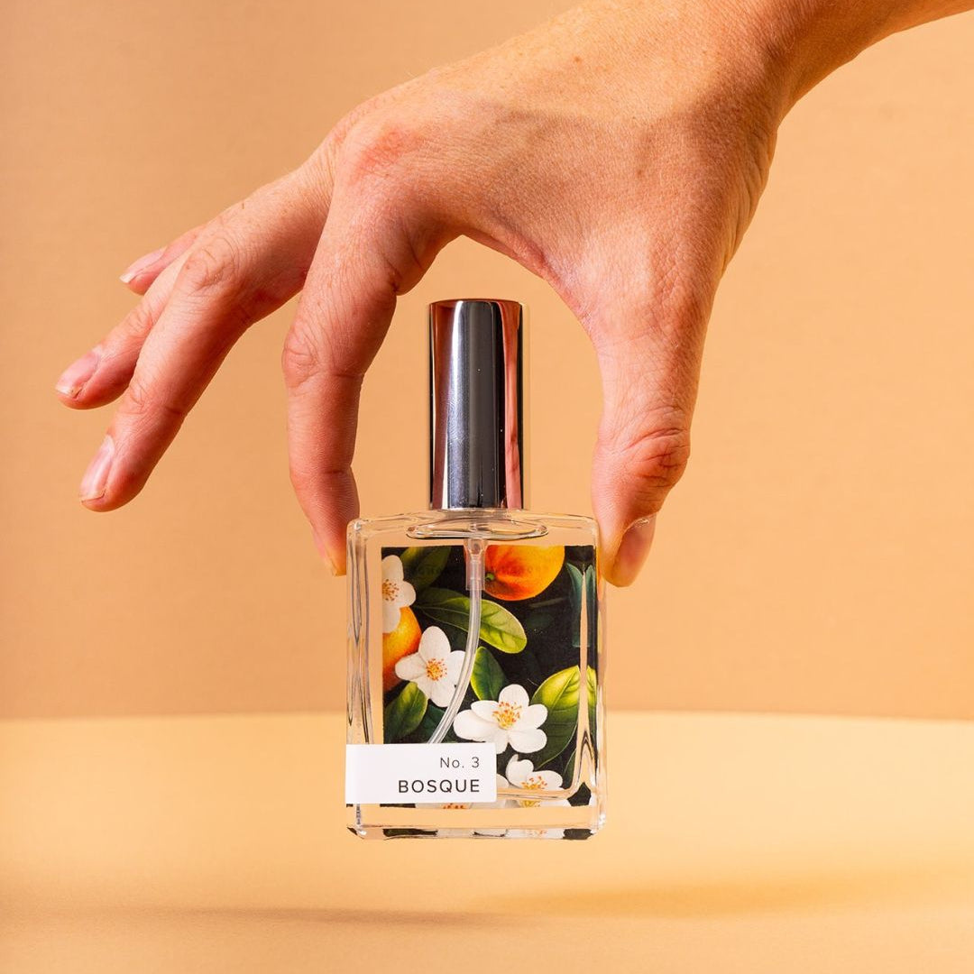 Hand holding Bosque Perfume in front of light orange background.
