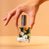 Hand holding Bosque Perfume in front of light orange background.
