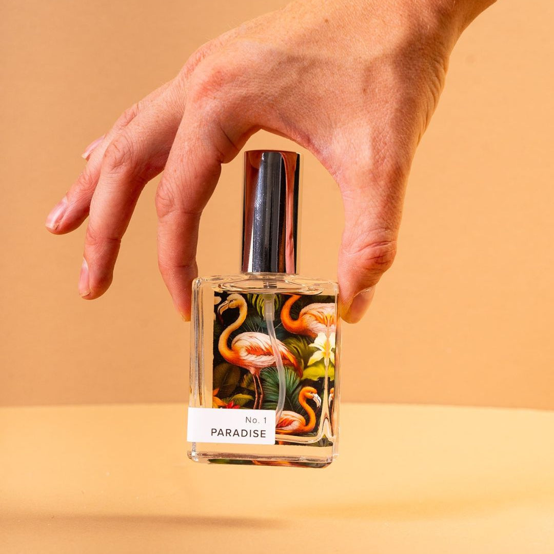 Hand holding Paradise Perfume on light orange background. 