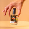Hand holding Paradise Perfume on light orange background. 