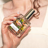 Woman holding Paradise Perfume in front of chest. 