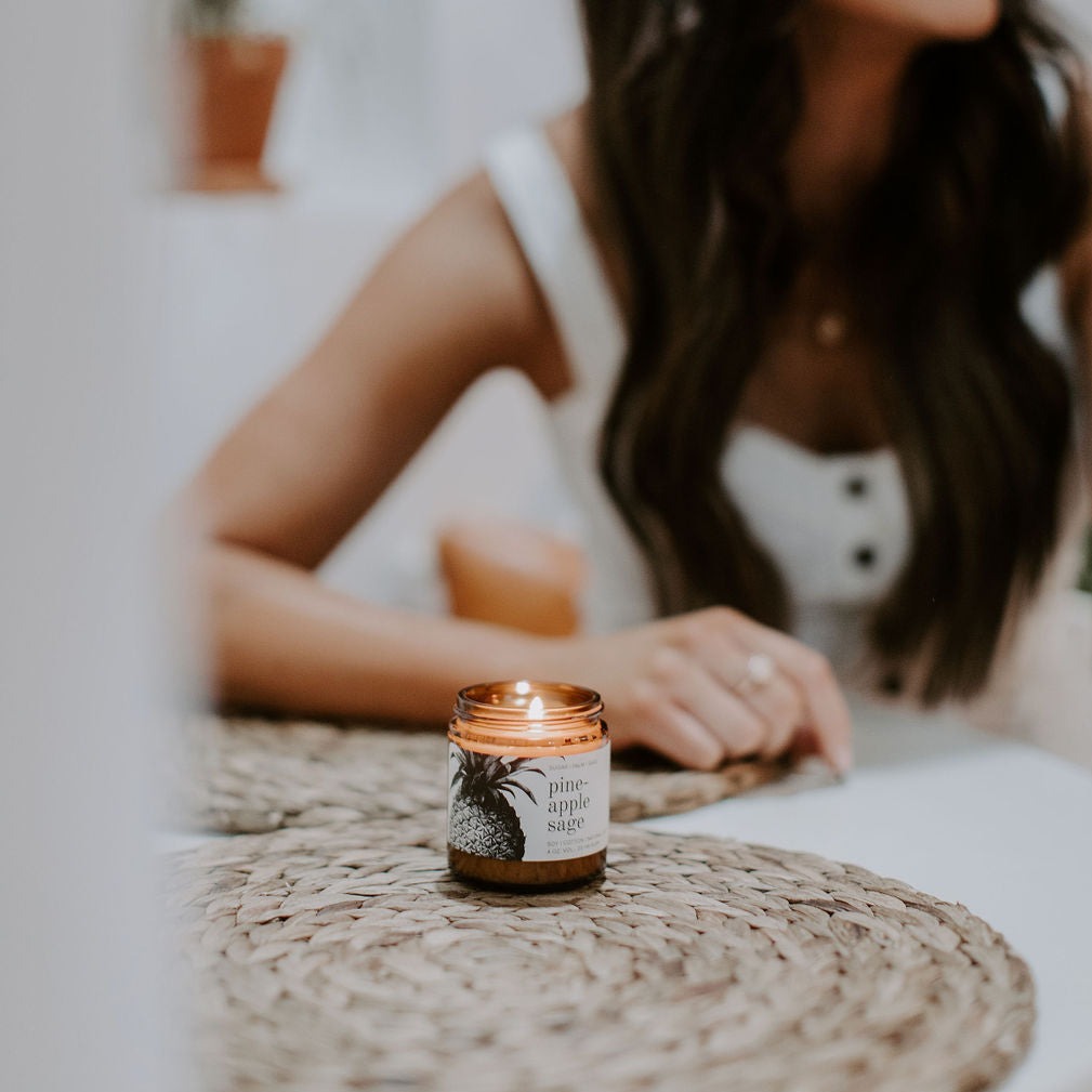 4oz Pineapple Sage Soy Candle on a placemat with a woman behind it. 