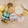 11oz French 75 Soy Candle on barrel with a bottle of Crater Lake Gin, lemons, and a French 75 cocktail. 