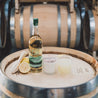 11oz French 75 Soy Candle on barrel with a bottle of Crater Lake Gin, lemons, and a French 75 cocktail. 