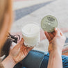 11oz Mint Mojito Soy Candle being held by one hand while the other hand holds a recipe for a Mint Mojito cocktail. 