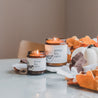 9oz and 4oz Pumpkin Spice Soy Candles on a table next to some decorative fall leaves. 